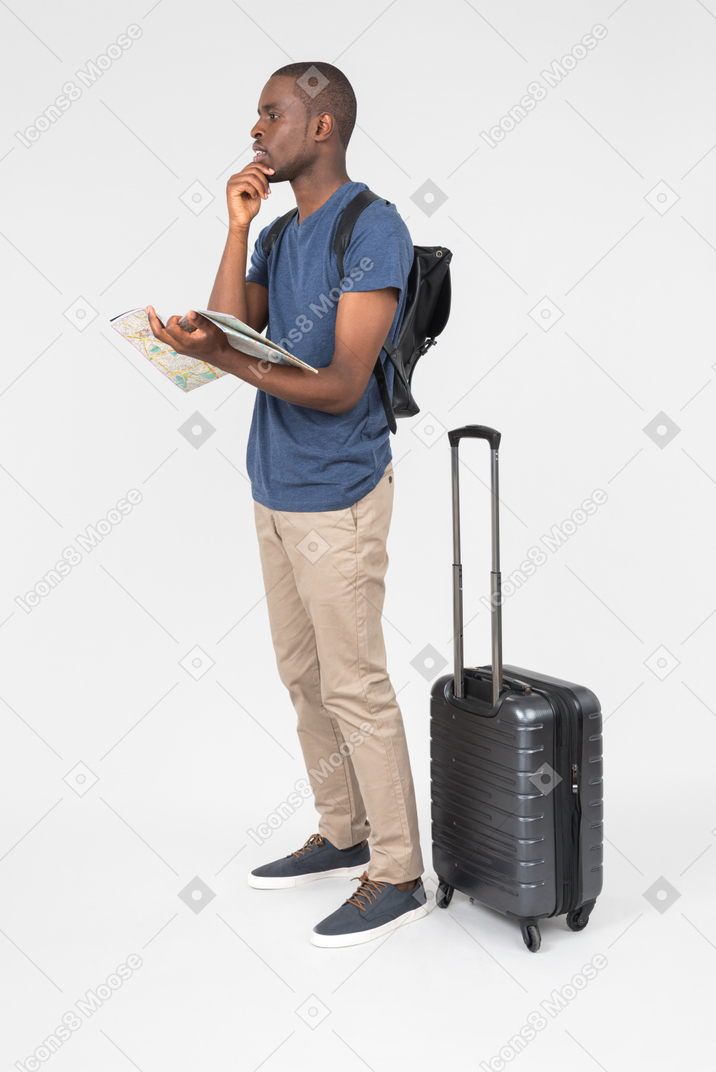 Pensive male tourist holding map and standing near luggage