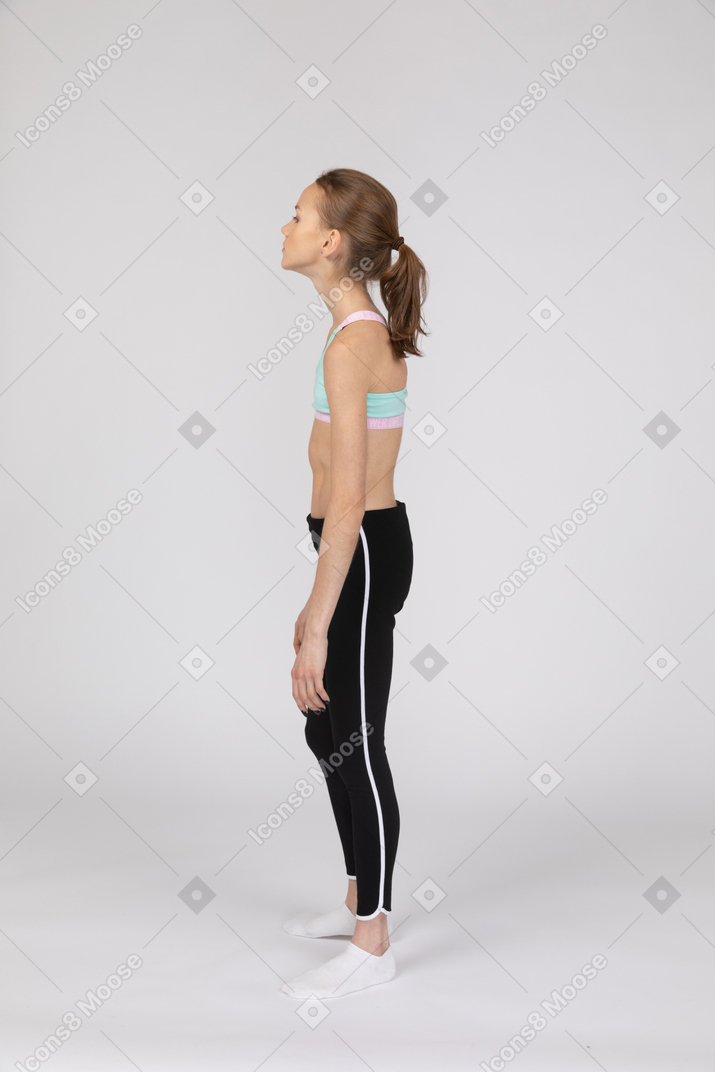Vista lateral de una jovencita cansada en ropa deportiva mirando hacia arriba