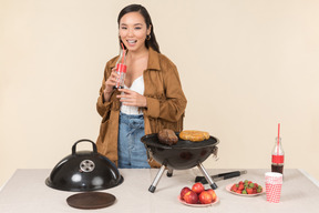 Laughing young asian woman holding coke and doing bbq