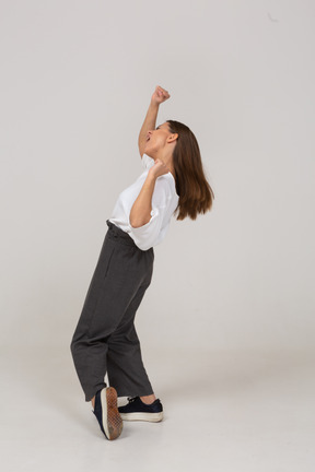 Vista laterale di una giovane donna che balla in abiti da ufficio alzando la mano