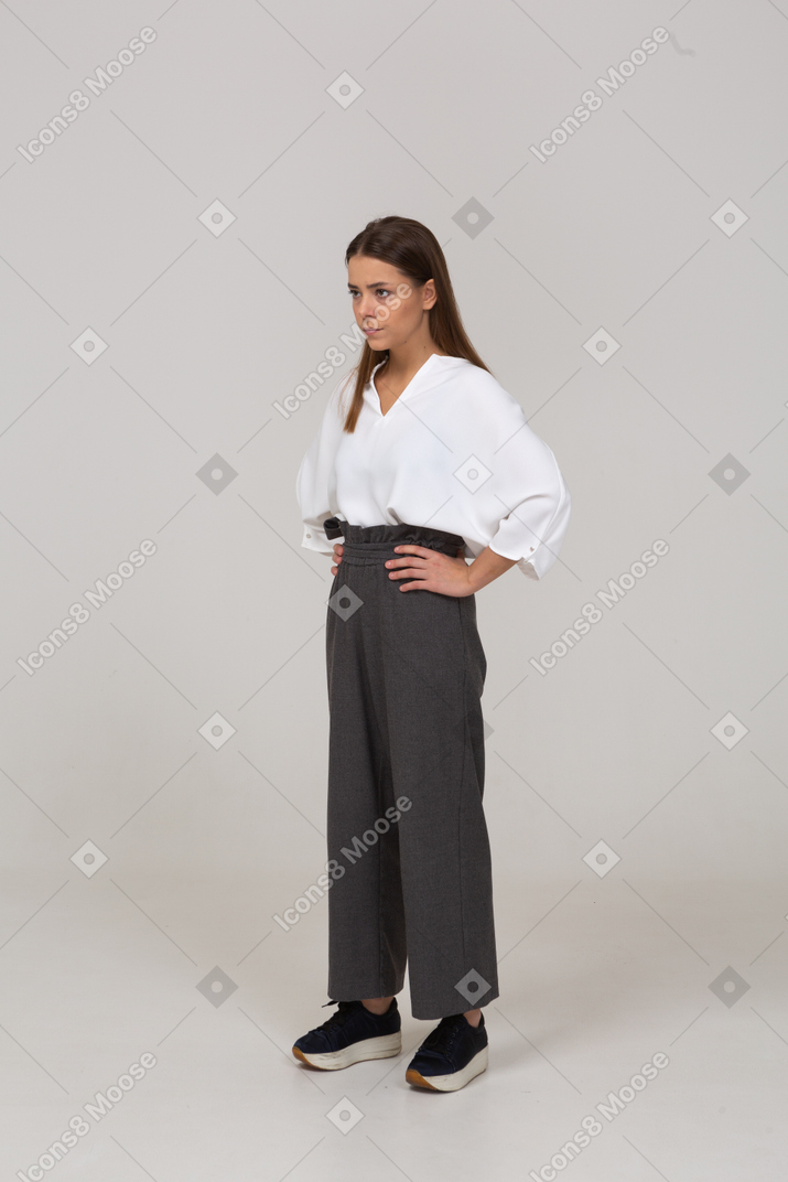 Three-quarter view of a serious young lady in office clothing putting hands on hips