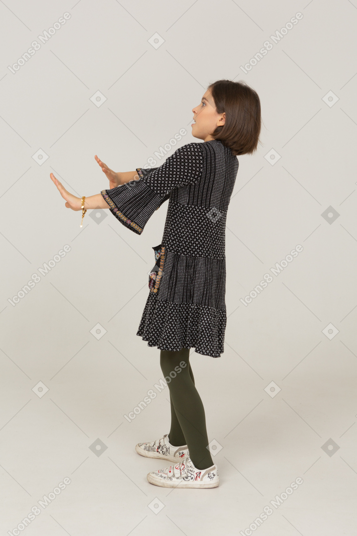 Vista lateral de una niña en vestido extendiendo sus brazos
