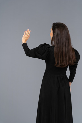 Back view of a young lady in a black dress raising her hand