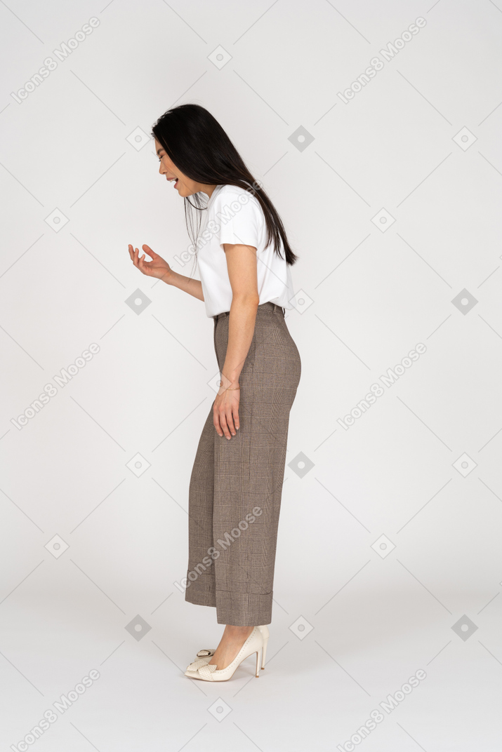 Vista laterale di una giovane donna urlante in calzoni e t-shirt alzando la mano