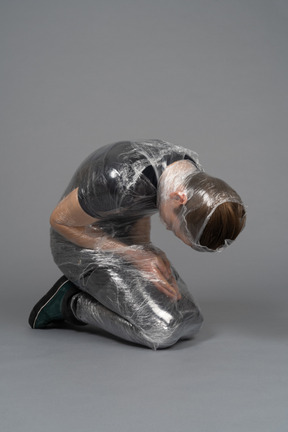 Young man on his knees wrapped in plastic