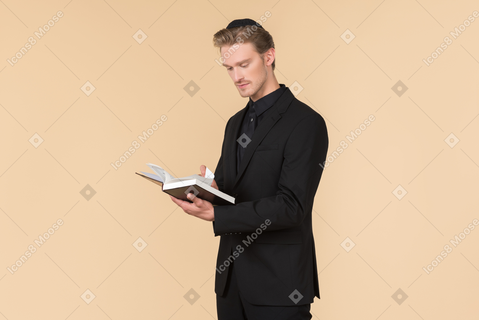 Young man in a black suit and a kippah reading a torah he's holding