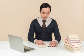 Молодой азиатский студент в свитере читает книгу