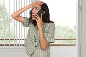 Surprised woman holding her head while talking on a phone