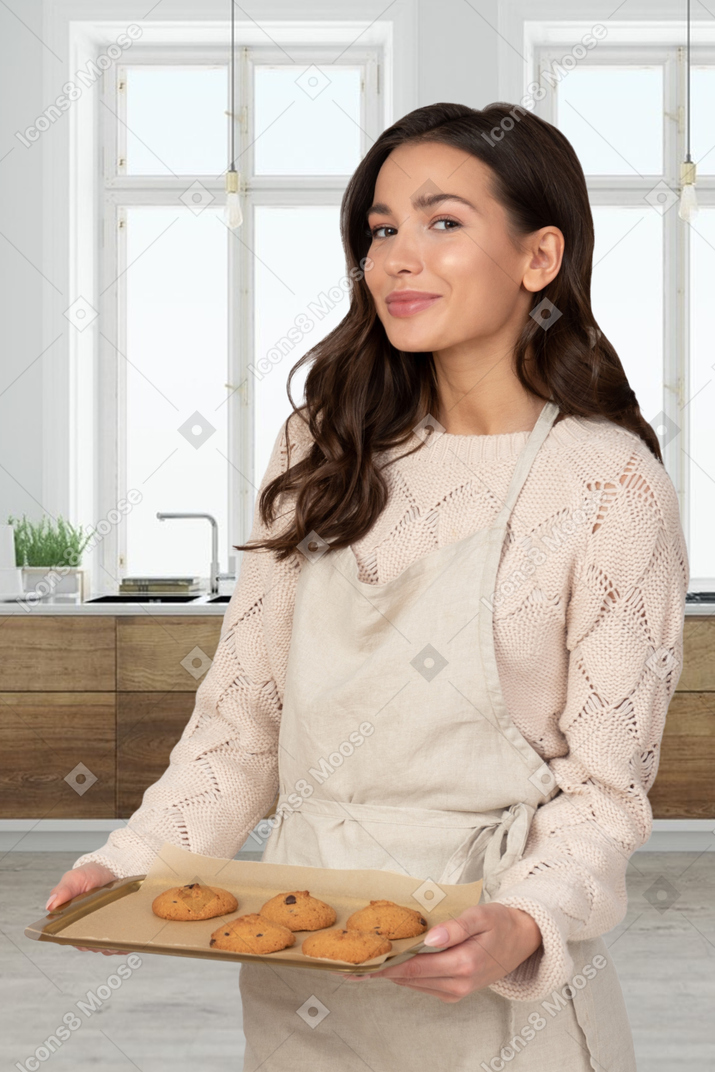 A woman in an apron holding a tray of cookies