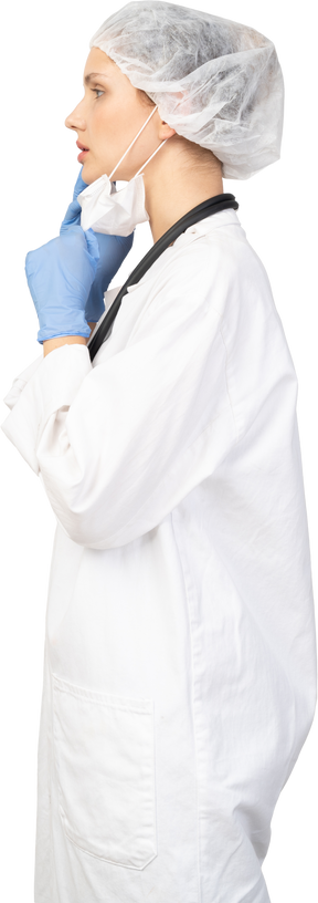 Vista lateral de uma jovem médica colocando uma máscara e olhando para o lado