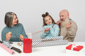 Abuelos y nieta sosteniendo hilos mientras envuelven regalos