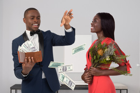 African woman holding bunch of flowers and young man throwing money bills