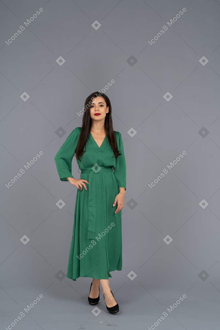 Vue de face d'une jeune femme en robe verte mettant la main sur la hanche