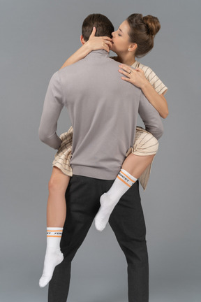 Back view of a young man holding his girlfriend up above the floor