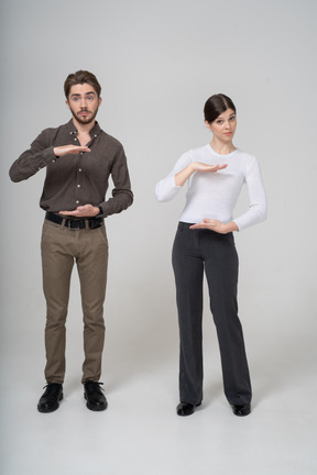 Vista frontale di una giovane coppia in abiti da ufficio che mostra le dimensioni di qualcosa