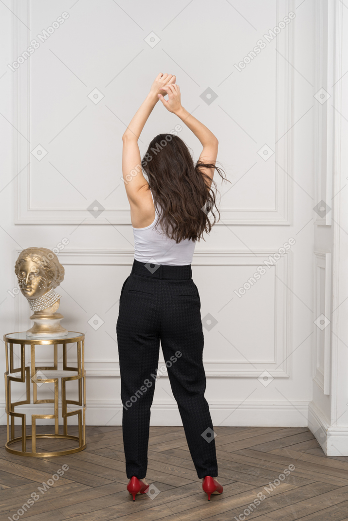 Back view of a young female raising hands while standing by a golden greek sculpture