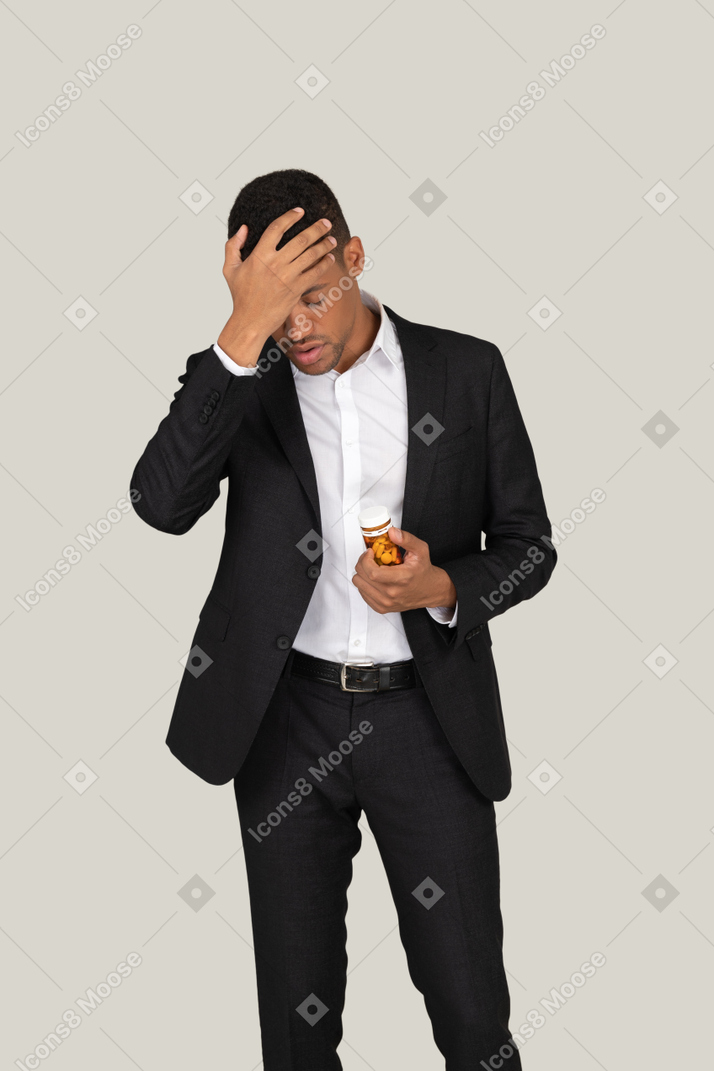 African american man in black suit holding pills bottle and covering his face with a hand