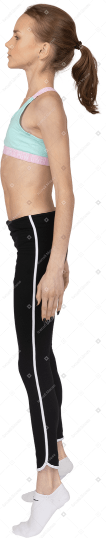 Девушка в спортивной одежде, стоя на цыпочках, вид сбоку