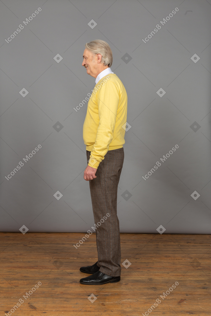Vista laterale di un vecchio uomo allegro in pullover giallo sorridendo e guardando da parte