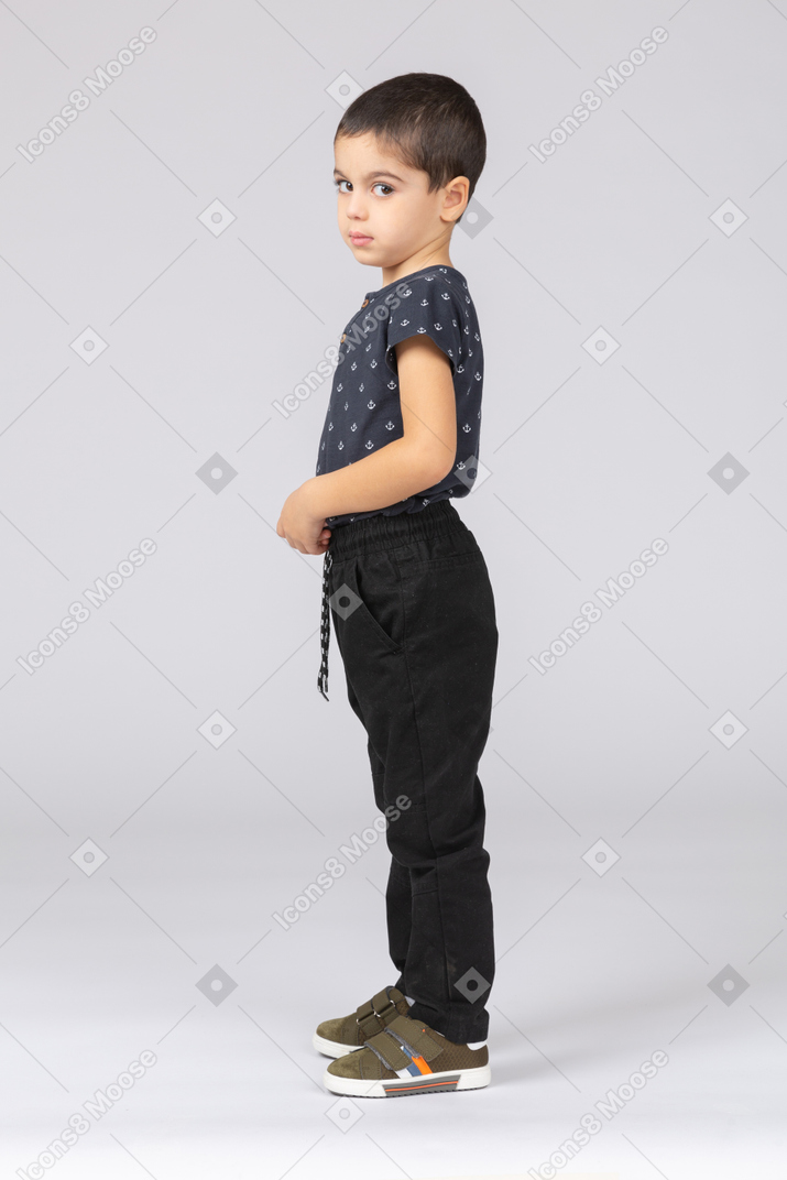 Garçon mignon dans des vêtements décontractés posant de profil et regardant la caméra