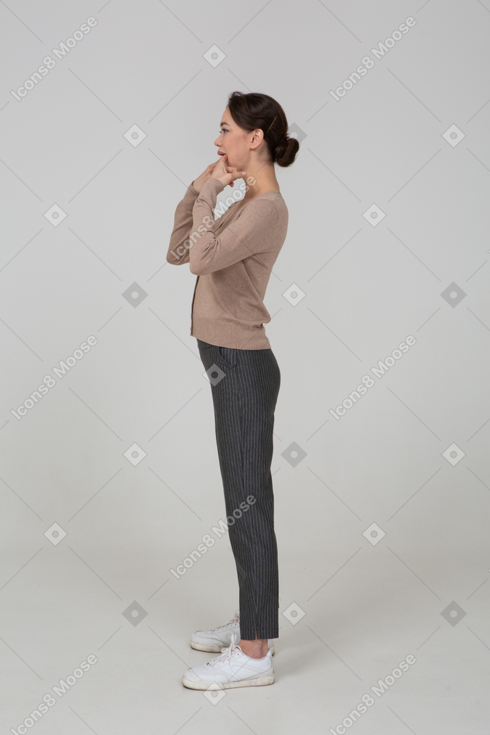 Side view of a young lady in pullover and pants touching her mouth