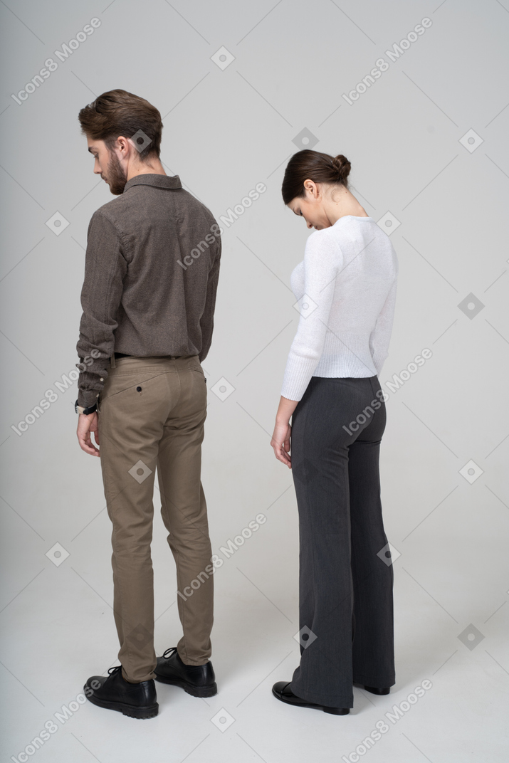 Three-quarter back view of a young couple in office clothing looking down