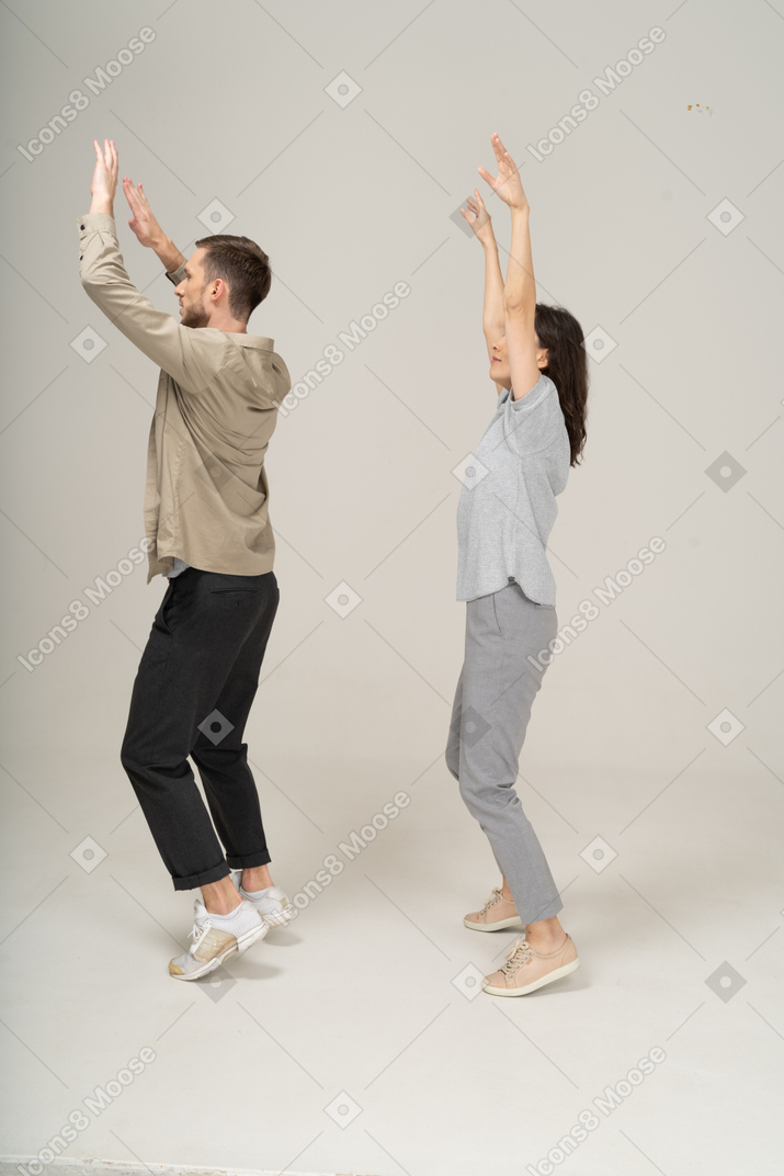 Vista lateral do jovem e da mulher com as mãos para cima