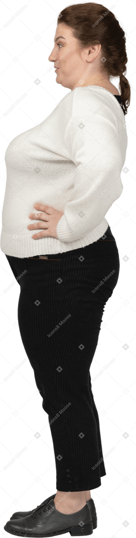Vista lateral de uma mulher plus size com roupas casuais em pé com as mãos na cintura