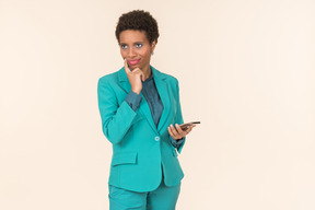 Jeune femme noire avec une coupe de cheveux courte, posant dans un costume bleu avec un téléphone portable à la main