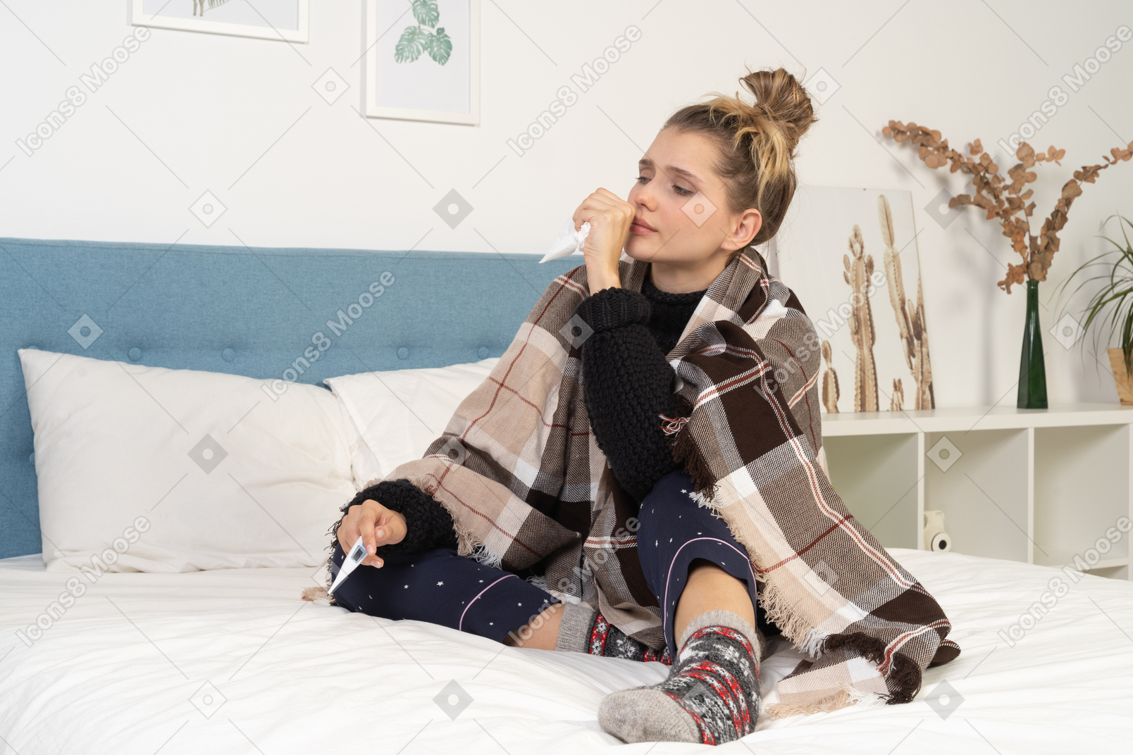 Front view of an ill young lady in pajamas wrapped in checked blanket in bed
