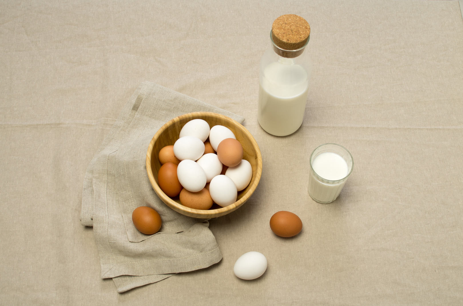 White and brown chicken eggs and some milk on a gray tablecloth