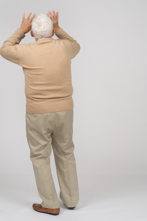 Vista traseira de um velho em roupas casuais em pé com as mãos levantadas