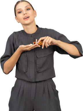 Front view of a smiling young woman in a jumpsuit pouring the pills out of a jar