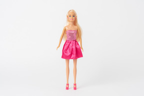 A front shot of a barbie doll in a shiny pink dress and pink high heels, standing isolated against a plain white background