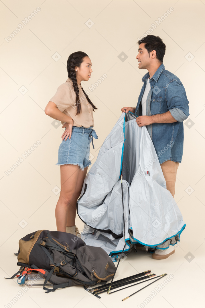 Young interracial couple arguing while setting up a tent