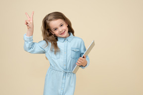 Cute little girl holding a tablet and showing v sign