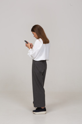 Vista traseira de três quartos de uma jovem com roupas de escritório, verificando o feed por telefone