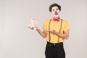 Smiling male clown pointing at toy rabbit he's holding