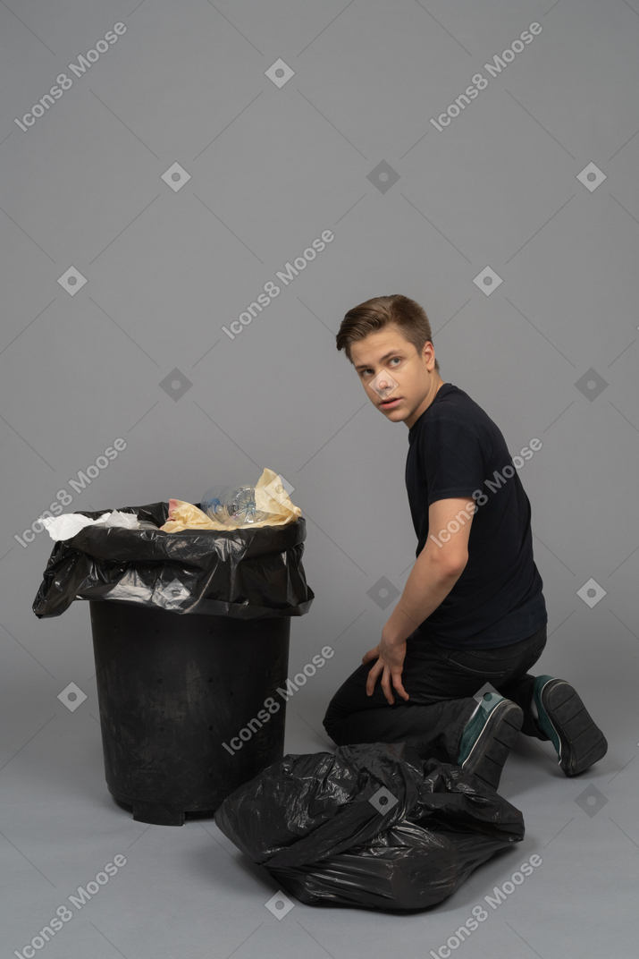 A young man sitting next to a waste bin