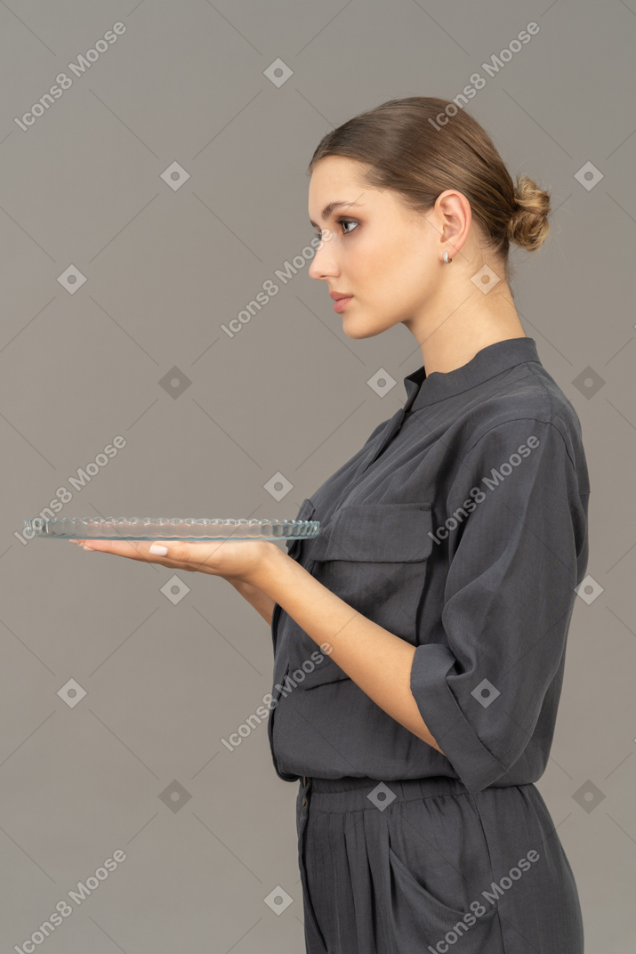 Вид сбоку молодой женщины в комбинезоне, держащей стеклянную тарелку