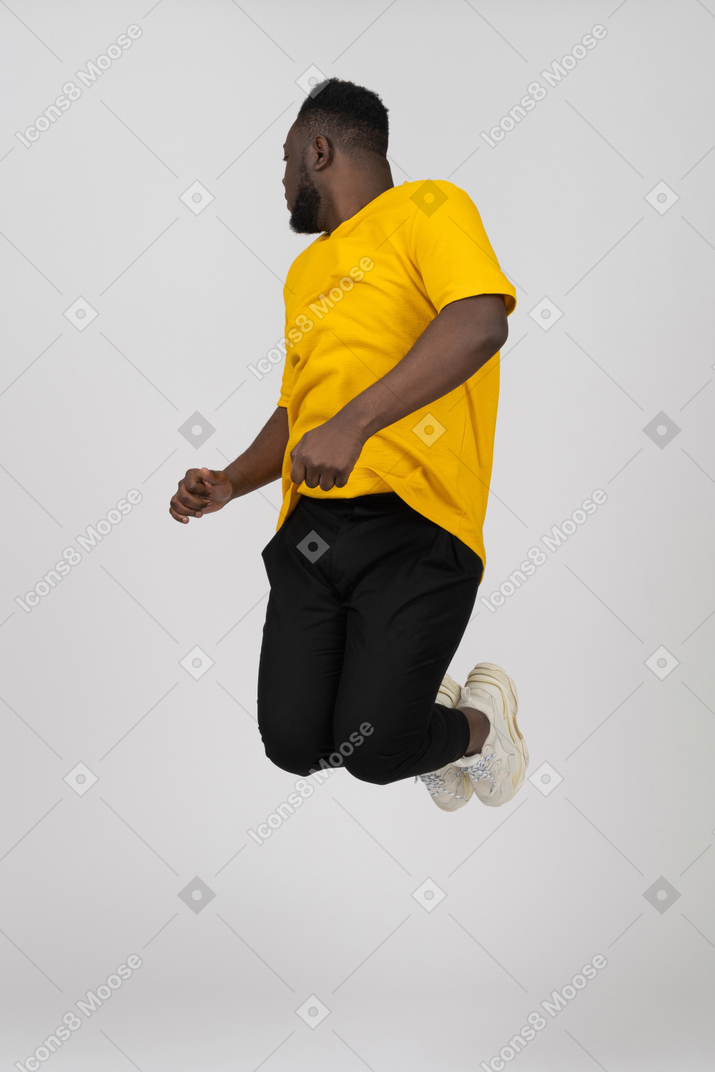 一个穿着黄色 t 恤的年轻深色皮肤男子跳跃的四分之三视图