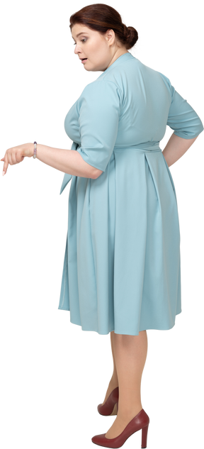 Vista lateral de una mujer en vestido azul apuntando hacia abajo con un dedo