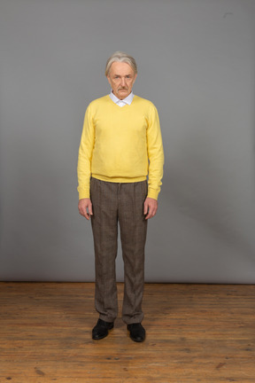 Vista frontal de um homem velho e triste de blusa amarela olhando para a câmera