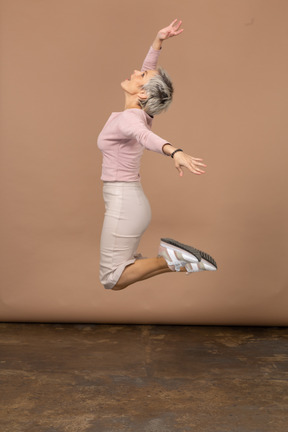 Vista lateral de una mujer feliz en ropa casual saltando con los brazos extendidos