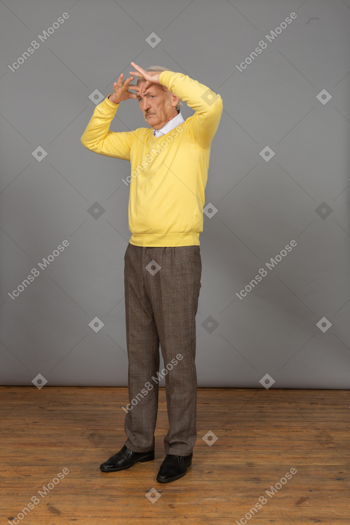 Three-quarter view of an old perplexed man in yellow pullover gesticulating actively and looking aside