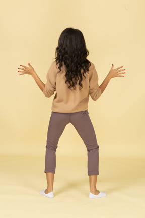 Back view of a funny dark-skinned young female outspreading her hands and legs