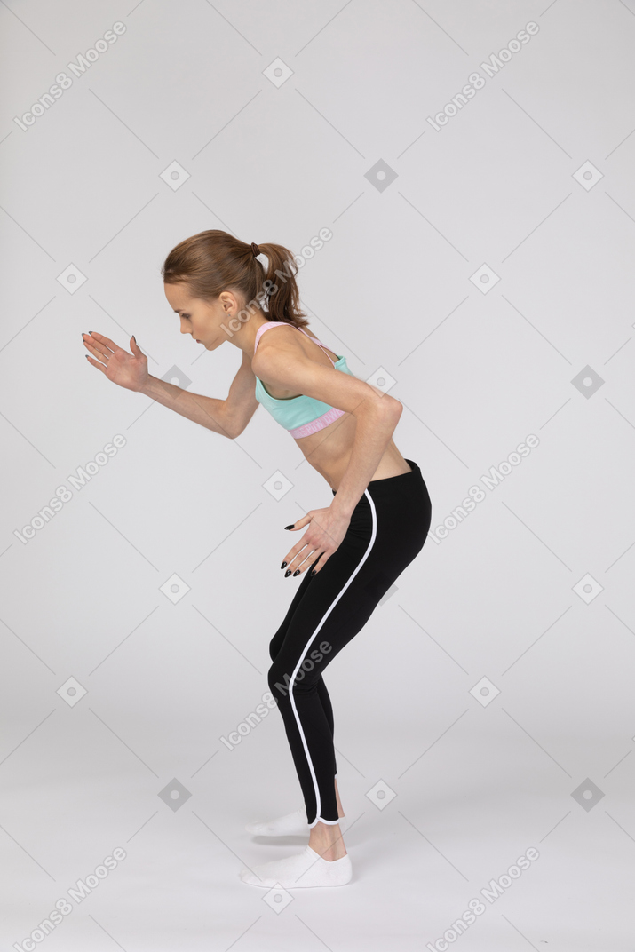 Side view of a teen girl in sportswear leaning forward while standing like a robot