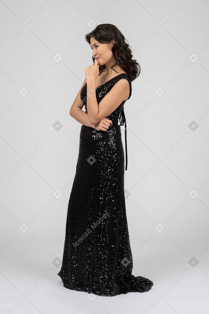 Женщина в черном вечернем платье стоит в профиль на камеру