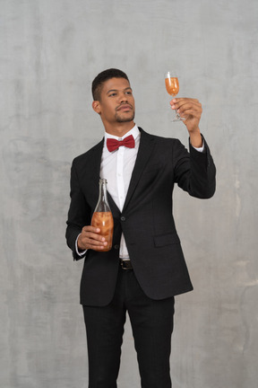 Homem com roupa formal, segurando uma taça de champanhe e olhando para ela