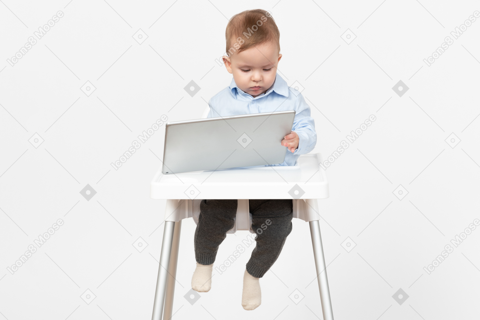 Adorable baby boy sitting in highchair and holding tablet